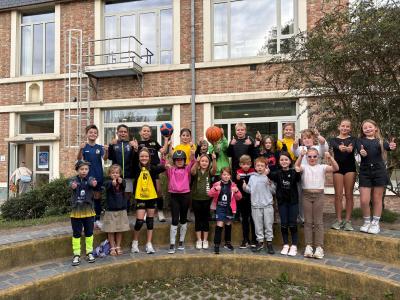 Kinderen staan in rijen opgesteld en steken hun duim in de lucht. Ze zijn uitgedost in de training van hun eigen sportclub.